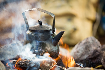 Man and woman making coffee in big kettle on campfire in forest on shore of lake, making a fire, grilling. Happy couple exploring Finland. Scandinavian landscape. 