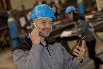 Happy factory male worker on the phone checking tablet at the sa