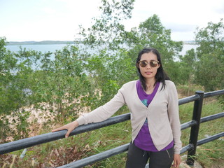 Asian woman wearing glasses, standing in the garden with a background of sea and trees