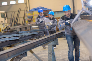 Male worker positioning a metal bar in metal factory