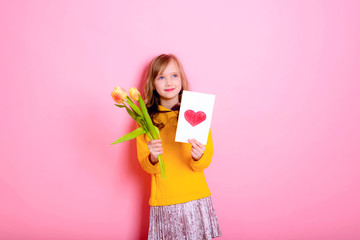 Happy Easter! Girl kid blonde in rabbit ears holding a card red heart, yellow tulips. Happy Mother's Day! International Women Day. Daughter's day.