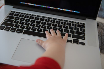 Educational concept. Female caucasian infant's hand using laptop computer at home, while sitting on mother's legs. Toddler family education on notebook or pc. view from back. view from back