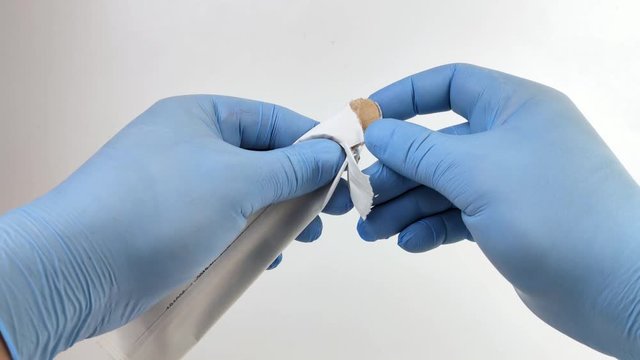 A doctor in blue medical gloves opens a disposable sterile medical spatula. Macro video of a wooden spatula for examining the oral cavity and tonsils.