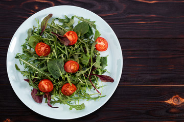 Rukula salad and tomatoes on a wooden background. View from above