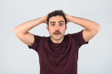 Foto op Plexiglas Worried and overwhelmed young man with a mustache with hand on his head. Purple t-shirt and isolated white background. © Lia Aramburu
