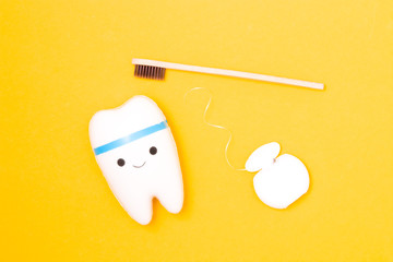tooth model, dental floss and bamboo toothbrush on yellow background, happy tooth, white healthy tooth, copy space, oral care concept