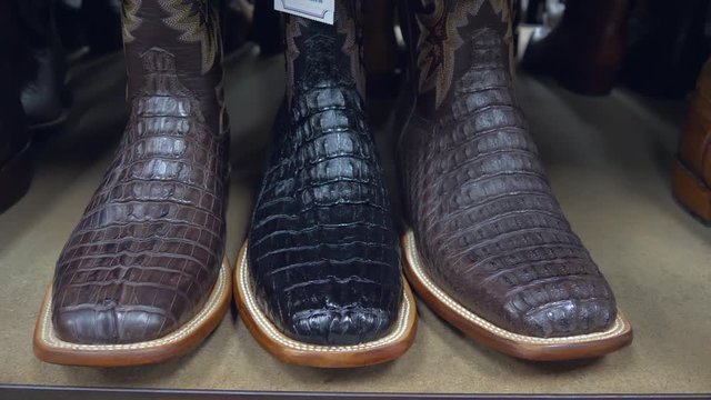 American-style boots from ostrich, crocodile and buffalo leather. Cowboy boots on a shelf in a store aligned, closeup. Side perspective close up on a pair of brown alligator leather cowboy boots.