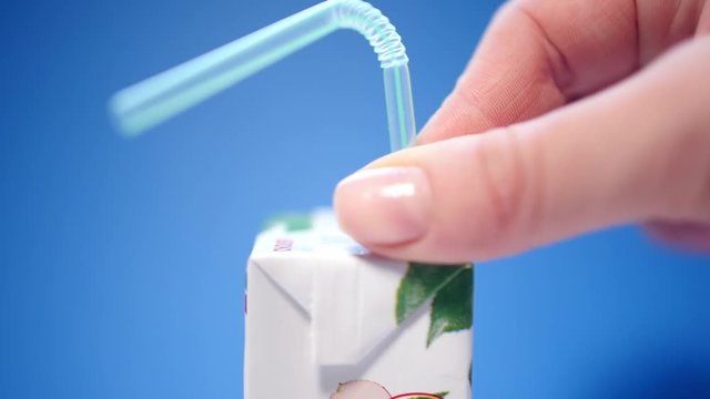 Closeup view of top of closed plastic small package with drink and female hand putting plastic straw inside of it. Real time full hd video footage.