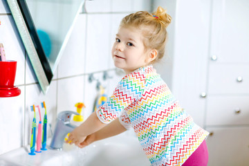 Cute little toddler girl washing hands with soap and water in bathroom. Adorable child learning cleaning body parts. Hygiene routine action during viral desease. kid at home or nursery.