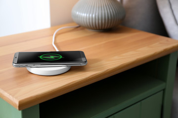 Smartphone charging on wireless pad in room. Space for text