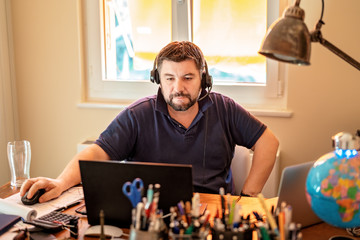 Man with headphones having conference call at home office. Working from home during quarantine and...