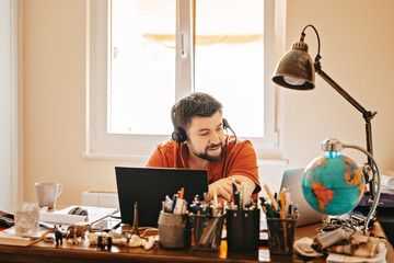Man with headphones and microphone having conference call online sitting at home office with two...