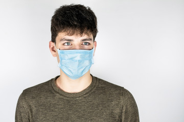 Guy with surgical medical mask on face on light background. The guy has a serious frightened face because he understands that a pandemic is dangerous
