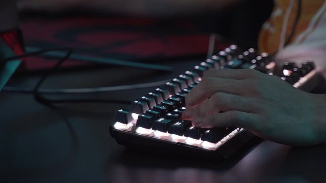Closeup shot of professional gamer hands playing on keyboard in dark room. Kyber sport concept