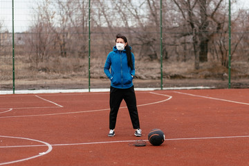 Obraz premium A young woman is playing sports on a sports field in a mask. Protection from coronavirus infection with a medical mask.