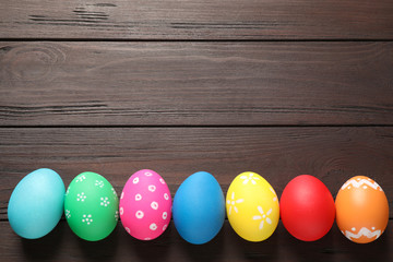 Colorful Easter eggs on wooden background, flat lay. Space for text