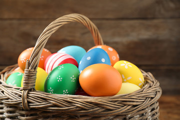 Colorful Easter eggs in basket on wooden background, closeup