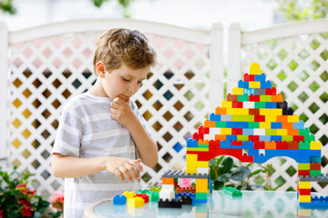 Little blond child and kid boy playing with lots of colorful plastic blocks.