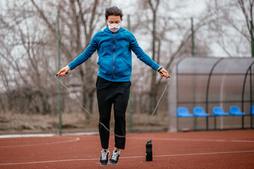 Fototapeta premium A young woman is engaged in jumping rope in a medical mask. Protection from coronavirus infection with a medical mask.