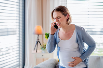 Portrait of pregnant woman in pain indoors at home, making emergency call.