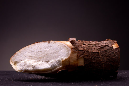 Edible Casava root with brown textured bark brightly lit in studio lighting contrasted against a dark grey background