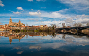 View of the Cathedral of Salamanca and the Enrique Estevan bridge reflected in the calm waters of the Tormes river