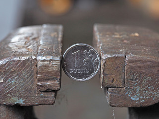 Coin one Russian ruble clamped by a metal vice on both sides. Concept of financial and business problems. The economy is in the grip