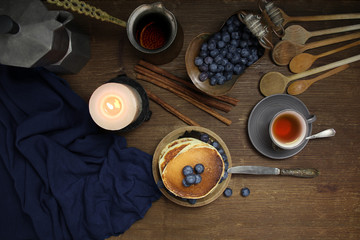 top view of a national dish fritters, pancakes, pita with blueberries, linen napkin, a candle burns, a cup of tea, an old mocha coffee machine, a concept of traditional cuisine