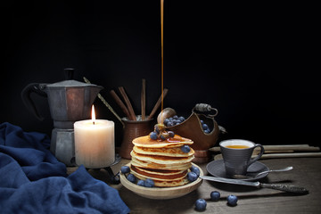 national dish pancakes, pancakes, pita with blueberries, honey pours on food, a linen napkin, a candle burns, a cup of tea, an old mocha coffee machine, a concept of traditional cuisine