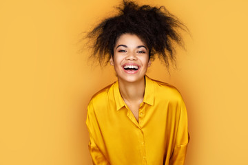 Fototapeta na wymiar Overjoyed girl can't stopping laughing. Photo of african american girl on yellow background