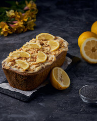 Vegan homemade lemon cake with poppy seeds and coconut sugar. White glaze with lemon slices and almonds. Selective focus. Dark photo style