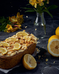 Vegan homemade lemon cake with poppy seeds and coconut sugar. White glaze with lemon slices and almonds. Selective focus. Dark photo style