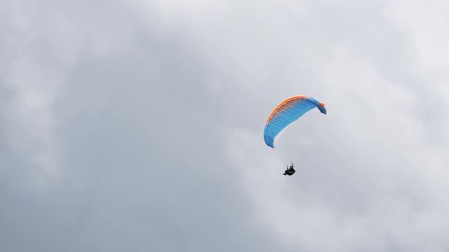 Paraglider flying in sky with clouds with parachute. Professional paragliding. A cloudy gray sky. Skydiver moves fast very high.