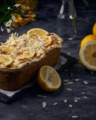 Vegan homemade lemon cake with poppy seeds and coconut sugar. White glaze with lemon slices and almonds. Selective focus. Dark photo style