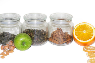 Dry green Indian and white Chinese loose leaf tea and cinnamon in glass jars with apple, orange and nuts on an isolated white background. Storage of tea leaves, cover for tea. copyspace