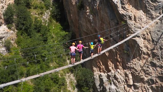 Active family on vacations. Tourists walk on suspension bridge, via ferrata in Alps. Hiking and climbing mountains, rocks. Weekend summer activity. Father and his three children.