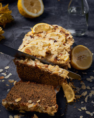 Vegan homemade lemon cake with poppy seeds and coconut sugar. White glaze with lemon slices and almonds. Selective focus. Dark photo style