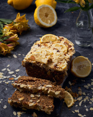 Vegan homemade lemon cake with poppy seeds and coconut sugar. White glaze with lemon slices and almonds. Selective focus. Dark photo style