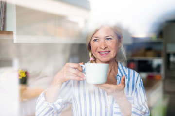 Portrait of senior woman with cup of coffee indoors at home.