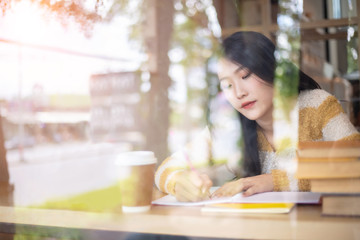 Young beautiful Asian woman reading a book while doing her homework in the modern co working space	