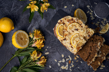 Obraz na płótnie Canvas Vegan homemade lemon cake with poppy seeds and coconut sugar. White glaze with lemon slices and almonds. Selective focus. Dark photo style
