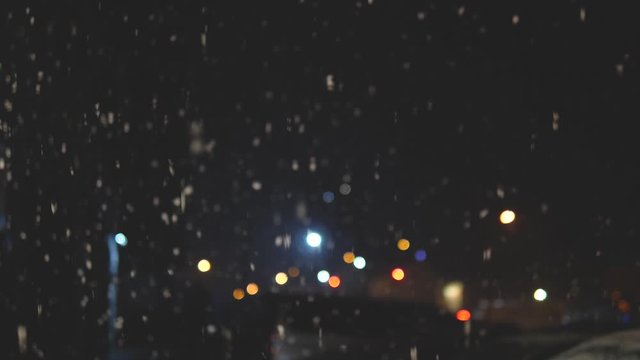 Snow flakes falling from the sky at night. Defocused street lights, snow falling in the dark at night.