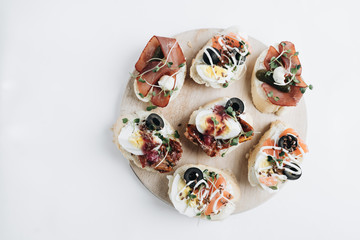 Delicious fresh bruschettas with eggs, salmon, olives and meat , traditional Italian cuisine, ingredients on white table 