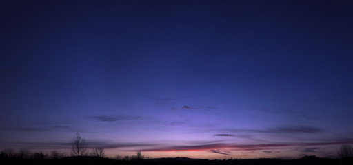 Beautiful blue, purple and orange twilight gradient sky during sunset in the early spring. Tree silhouettes, stitched panorama.	