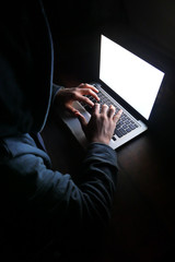 hooded hacker stealing data from laptop at night 
