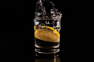 Splash in a glass with lemon on a black background. Fresh healthy drink concept
