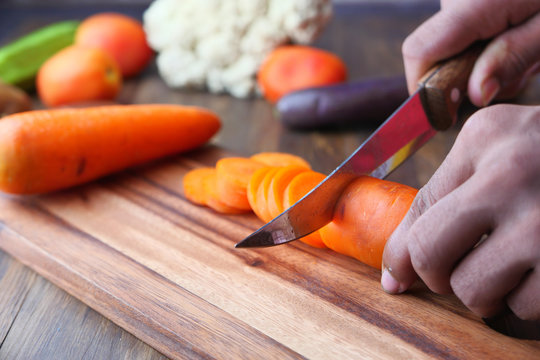 Closeup image of a man cutting and chopping carrot by knife on wooden board