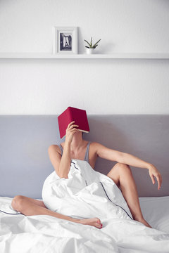 Frau mit rotem Buch auf dem Gesicht im Bett