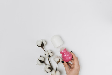  female hand holding pink deodorant on white background, armpits care, cotton flowers