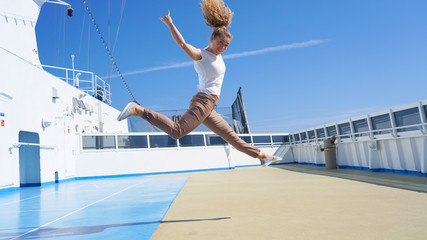 Rock sign performed by a curly curly girl. beautiful sporty girl on the deck of a cruise ship jumps Sign of the horns. Emotion fun joy on a sunny day. rest on a cruise ship. vacation
